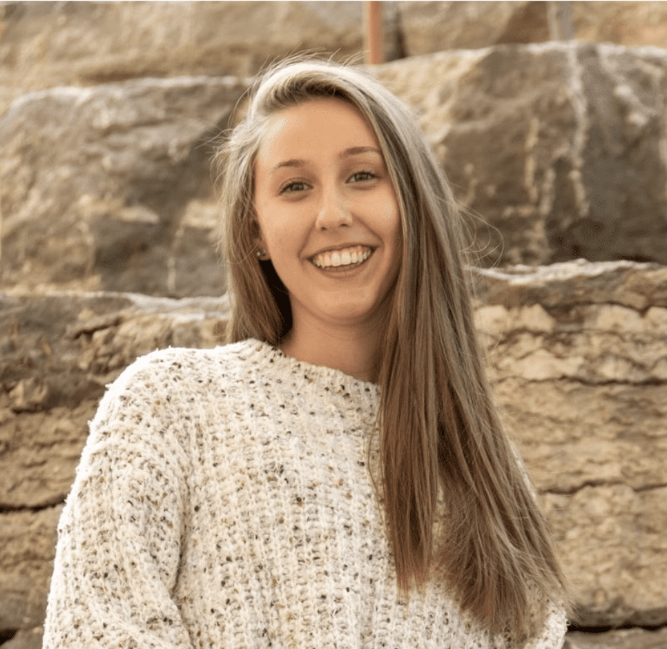 A woman with long hair standing in front of a rock wall.